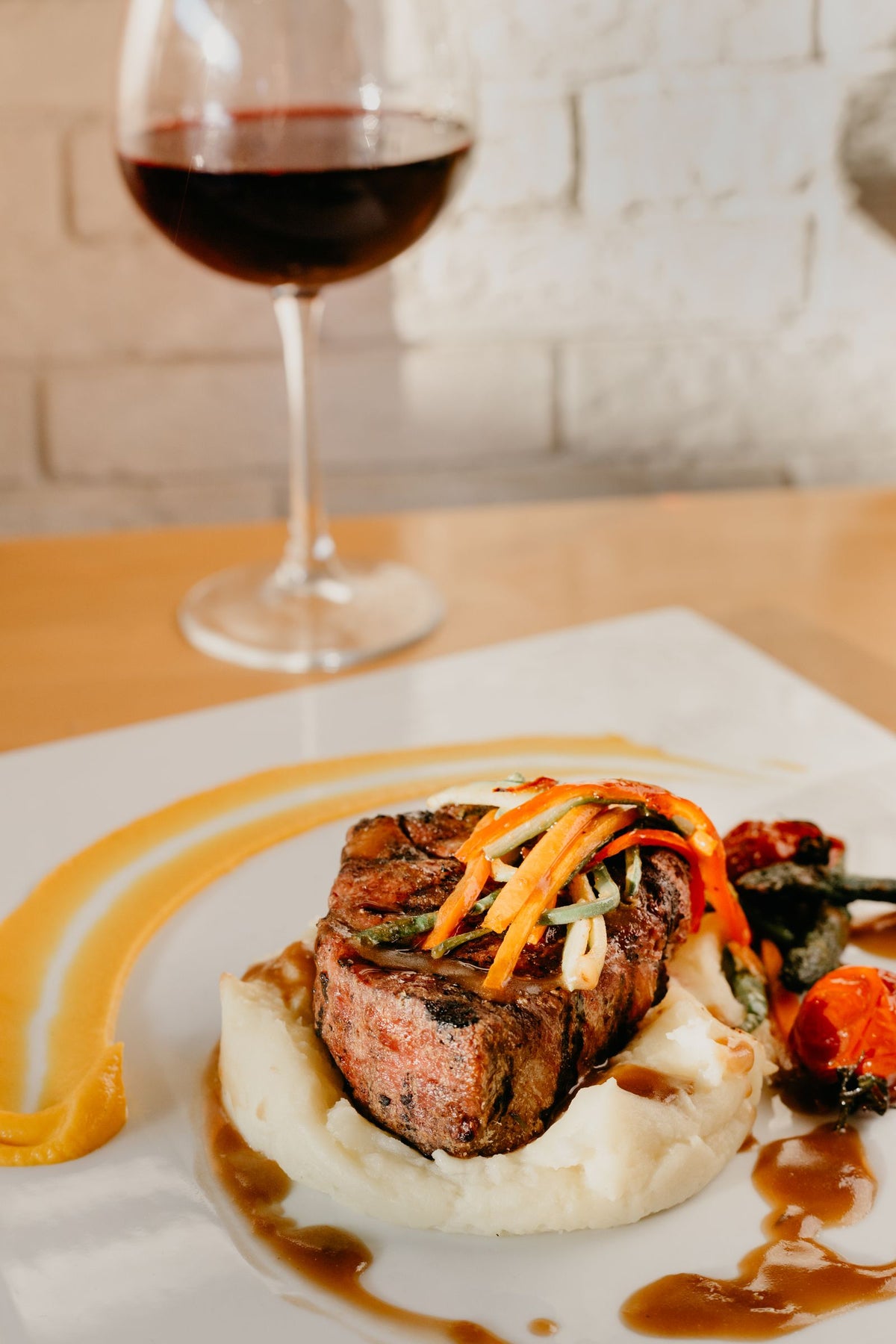 A grilled steak plated with vegetables beside a glass of red wine