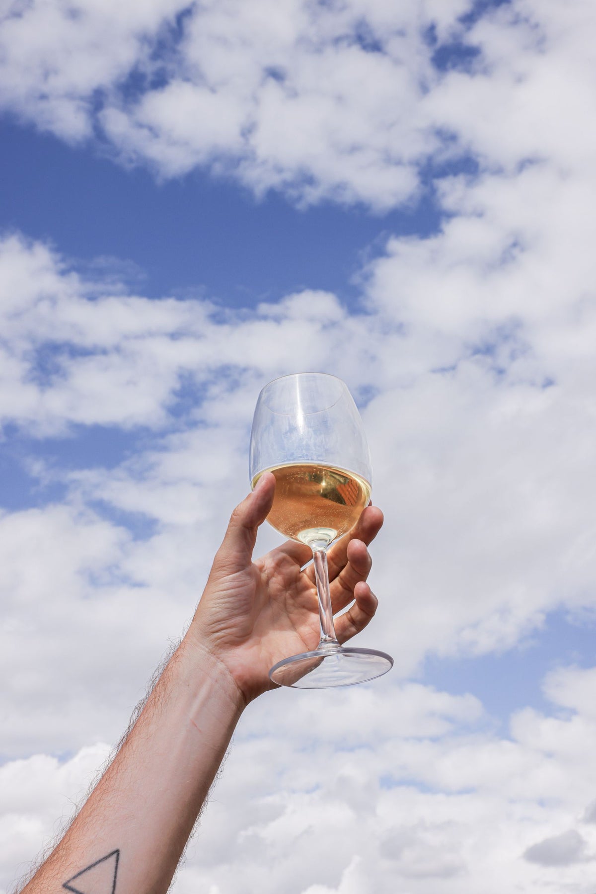 Low angle view of a hand holding a glass of white wine against a bright blue sky