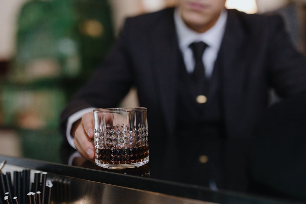 Man in a suit holding a whiskey glass at a bar counter
